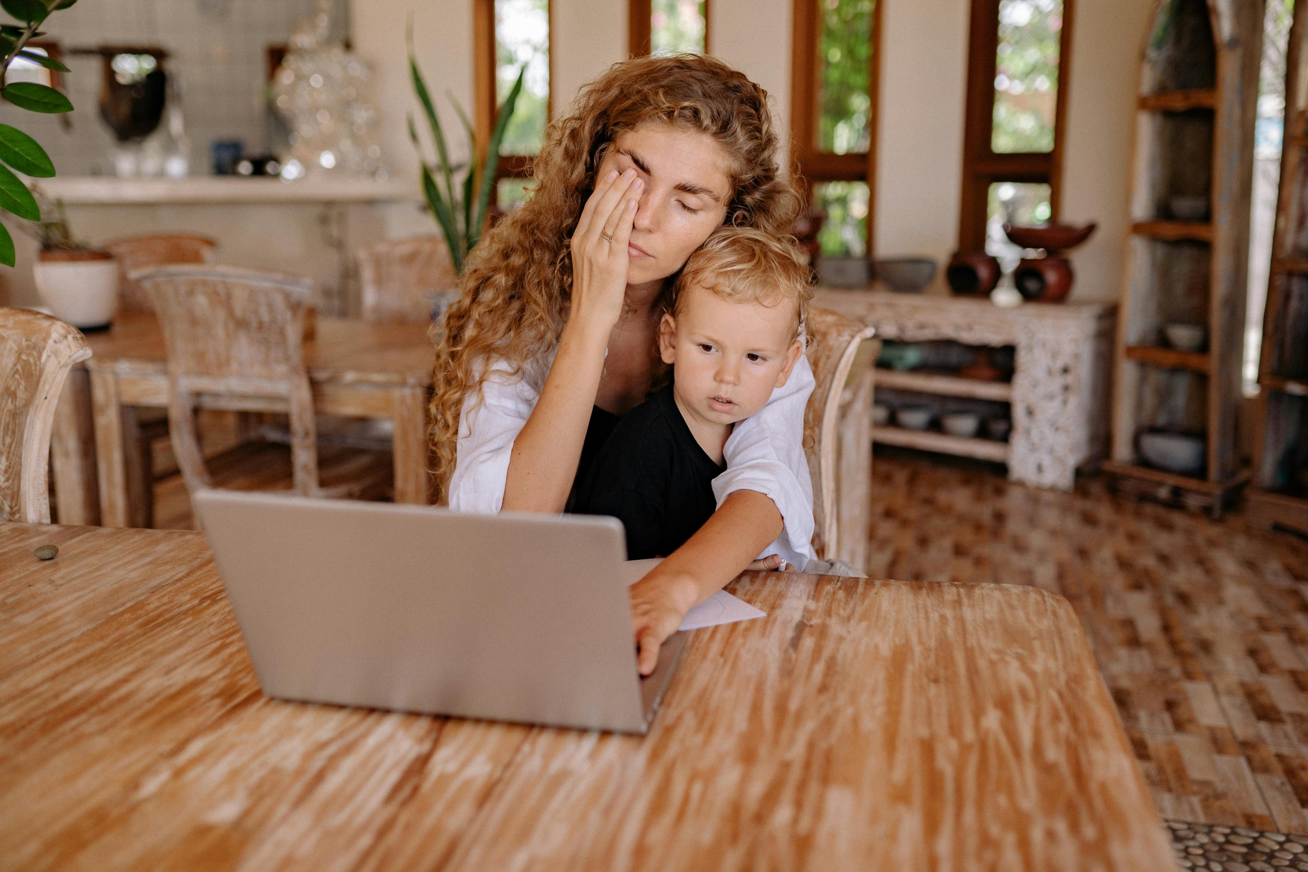 Stessed out mom holding a baby while sitting at the computer.