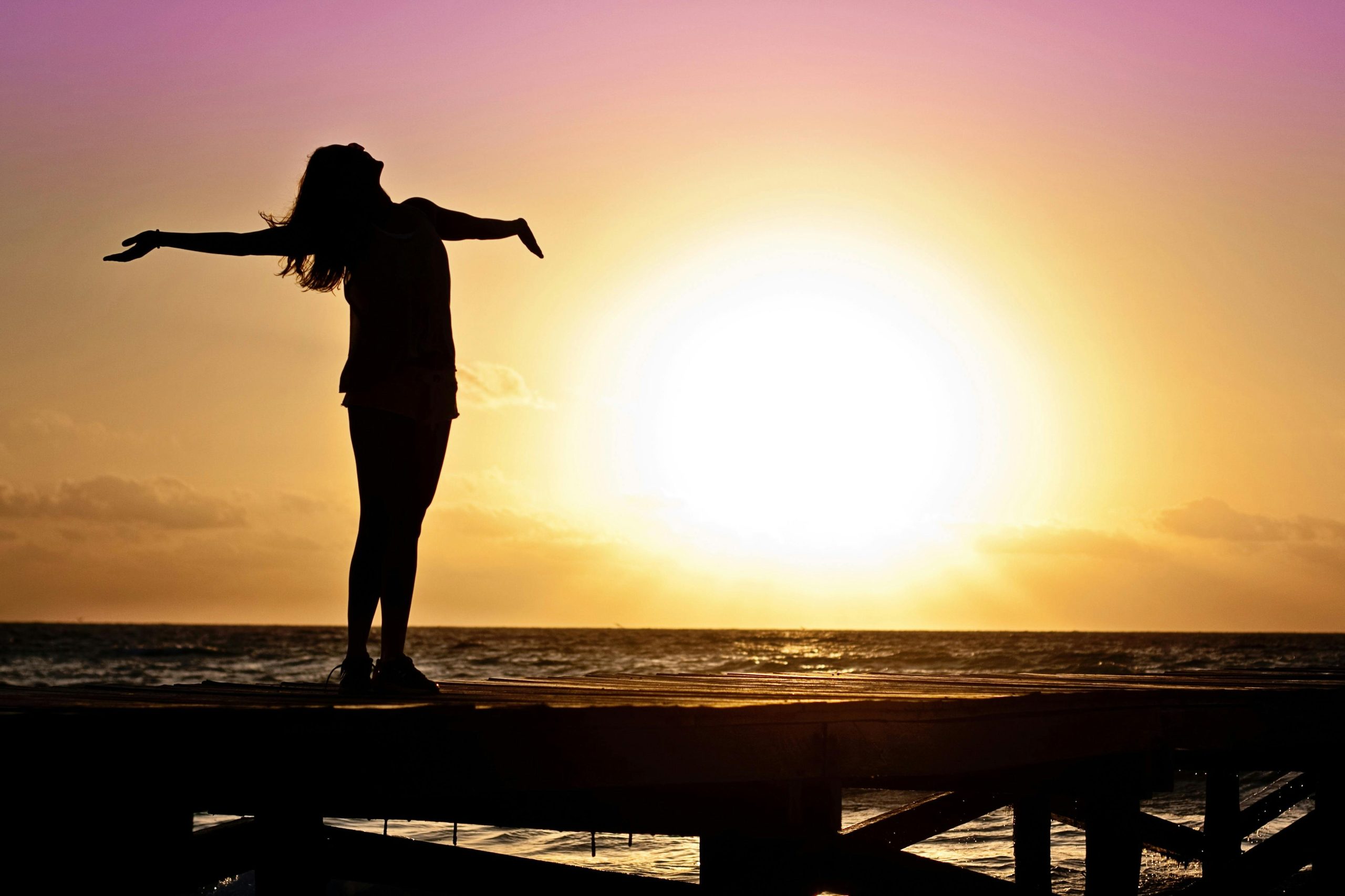 Person opening up to the sun while looking at the ocean.